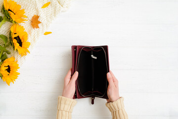 Woman hands holding open empty burgundy leather wallet on wooden table after autumn sale