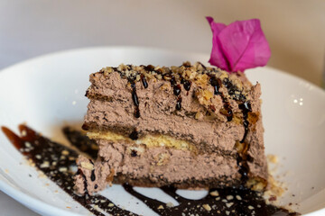 Portion of truffle chocolate tart decorated with a  purple flower on white plate. 