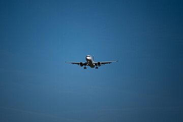 A landing commercial airplane set against blue sky background. Looking up, close up telephoto shot