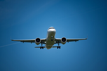 A landing commercial airplane set against blue sky background. Looking up, close up telephoto shot