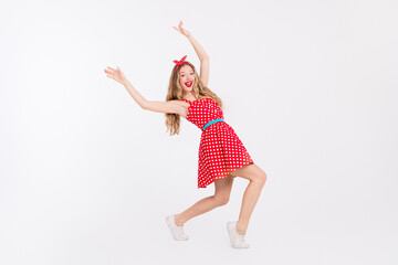 Energetic young woman in vibrant retro polkadot fashion striking a cheerful pose against a white...