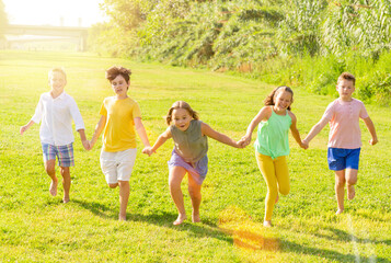 Fototapeta premium Glad young boys and girls running on green grass on field.