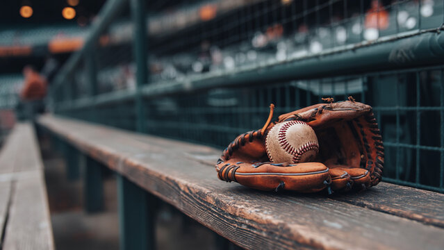 Close-up of a baseball inside a leather glove on a bench in an empty stadium, with blurred background