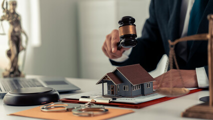Miniature house, foreclosure auction, lawyer, wooden hammer on table with blurred house in background. Real estate auction and foreclosure concept