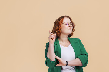 Joyful woman with red hair in green jacket against orange background says no and raises finger