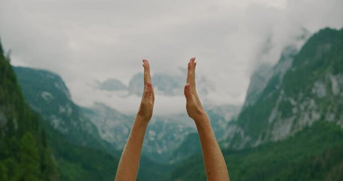 Hands in a yoga prayer pose against a serene mountain landscape with clouds