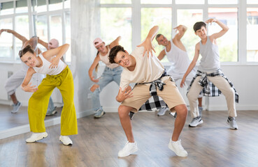 During rehearsal workout, teenage guy dances hip hop with friends against background of large...