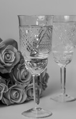 Black and white vertical photo of two glasses and roses on a light background, romantic setting, side view