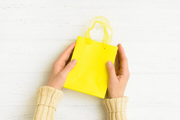 Yellow paper bag in woman's hands over wooden table. Top view