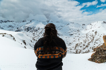 Woman in patterned fleece stands on snowy cliffside overlooking Sierra de Gredos mountains in Spain...