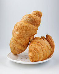 Two fluffy croissants in a white plate on white background.