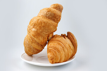 Two fluffy croissants in a white plate on white background.