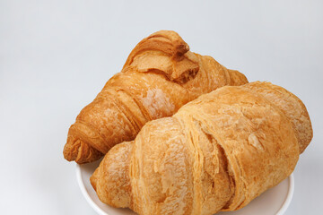 Two fluffy croissants in a white plate on white background.