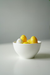 Minimal Easter composition with yellow and white eggs in a glossy ceramic bowl on a white surface. Bright and clean image perfect for spring holidays, decoration, and seasonal design.