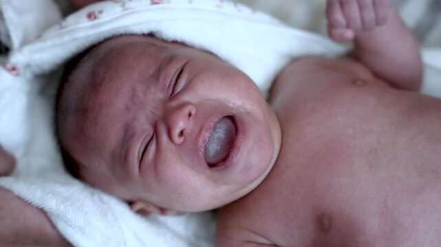 Newborn baby crying while laying down on a white towel after bath, showing sadness and discomfort