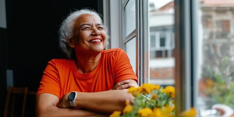Elderly african female in orange shirt smiling by window, embracing joyful moments