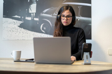 Woman working remotely on laptop with headphones in modern home office.