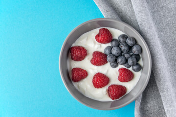 Gray bowl and natural yogurt with berries on the blue background.