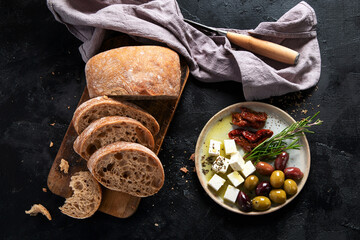 Olive oil and olives in bowls, sliced bread and rosemary on cutting board.