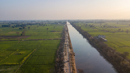 Aerial view of serene BRB Canal surrounded by expansive green fields and tranquil farmland, Lahore, Punjab, Pakistan.