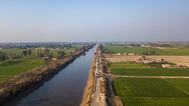 Aerial view of BRB Canal surrounded by lush fields and rural homes, Lahore, Punjab, Pakistan.