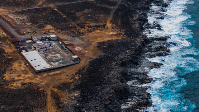 Aerial view of seawater desalination plant on a rugged volcanic coast with crashing waves, Lanzarote island, Canary Islands, Spain.