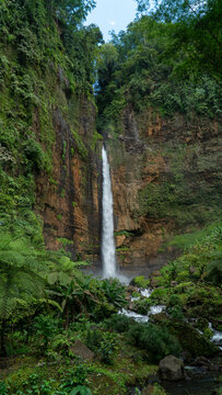 Aerial view of kapas biru waterfall cascading down a lush green cliff surrounded by serene forest, Lumajang, East Java, Indonesia.
