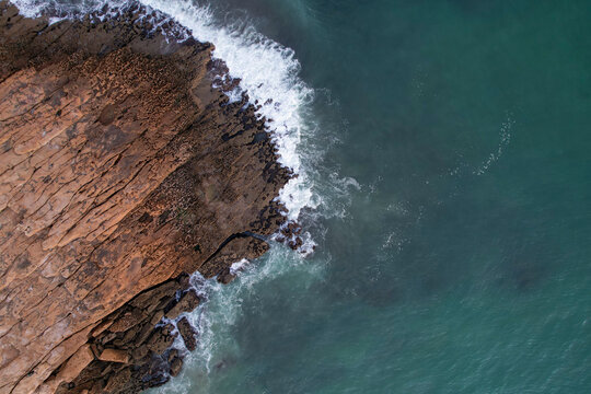 Aerial view of beautiful cliffs and rugged rocks along a pristine coastline with turquoise ocean waves, Algave, Portugal.