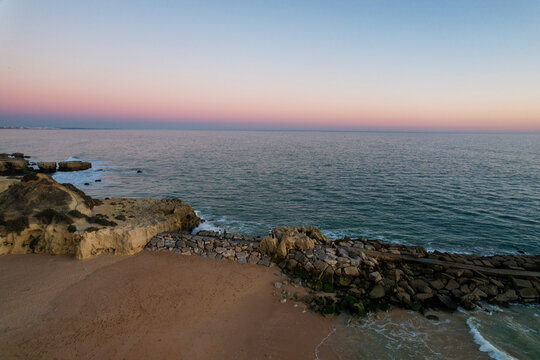Aerial view of beautiful beach with tranquil ocean and scenic coastal rocks at sunset, Algave, Portugal.