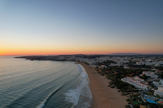 Aerial view of beautiful sandy beach and tranquil ocean at sunset with picturesque shoreline and residential buildings, Algave, Portugal.