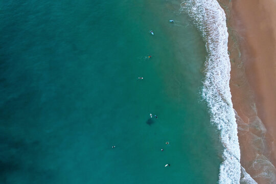 Aerial view of beautiful sandy beach with tranquil ocean waves and people enjoying summer activities, Algave, Portugal.