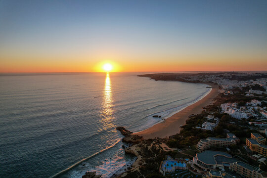 Aerial view of beautiful sunset over tranquil beach and ocean with coastline and buildings, Algave, Portugal.