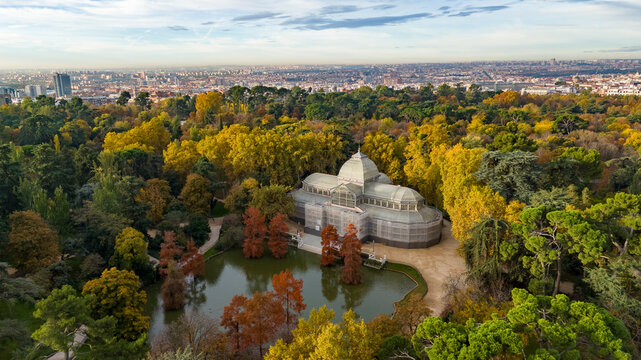 Aerial view of Parque el Retiro with the beautiful Palacio de Cristal surrounded by vibrant autumn foliage and a serene pond, Retiro, Madrid, Spain.