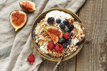 Homemade granola with yogurt, figs and berries on wooden background. Healhty breakfast. Top view