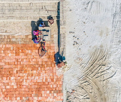 Aerial view of a brick factory with workers and bicycles amidst dust and patterns, Dhaka, Dhaka, Bangladesh.