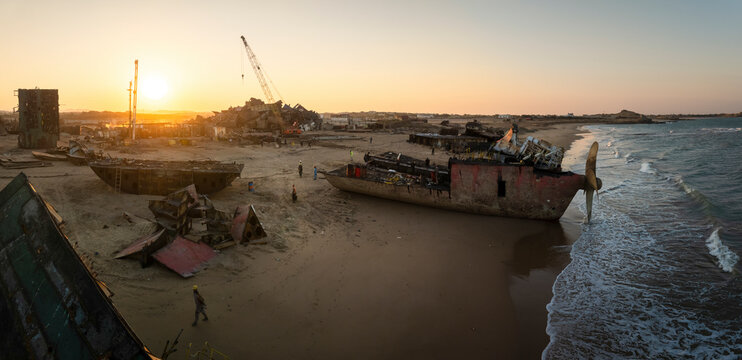 Aerial view of ship breaking yard at sunset with shipwrecks and cranes along the coast, Balochistan, Pakistan.