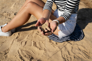 A young woman sits on the sand, gently letting grains of sand slip through her fingers, enjoying a sunny beach day