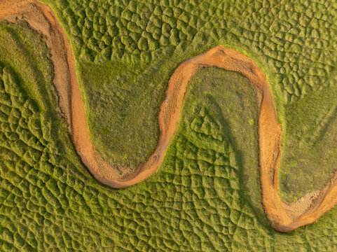 Aerial view of a winding yellow river surrounded by lush green grass and natural landscape, Olfus, Southern Region, Iceland.
