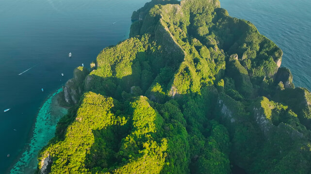 Aerial view of a picturesque tropical island surrounded by clear blue water and lush greenery with rocky cliffs, Phi Phi, Krabi, Thailand.