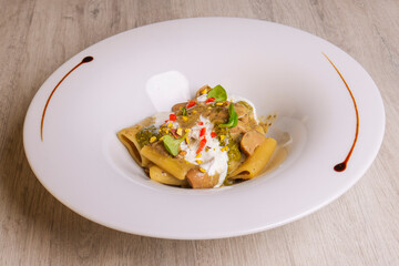 Paccheri con funghi, pesto di pistacchio e stracciata di bufala serviti in un ristorante come primo piatto