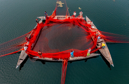 Sariakandi, Bangladesh - 17 February 2020: Aerial view of fishermen using a huge red net on tranquil water with boats, Sariakandi, Rajshahi, Bangladesh.