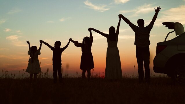 Big family at sunset holding hands, silhouettes. Happy people children parents lined up according to height held hands raised in air with joyful cheerful feeling of freedom anticipation of journey.