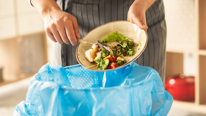 Woman scraping leftover food from plate into trash bin in kitchen