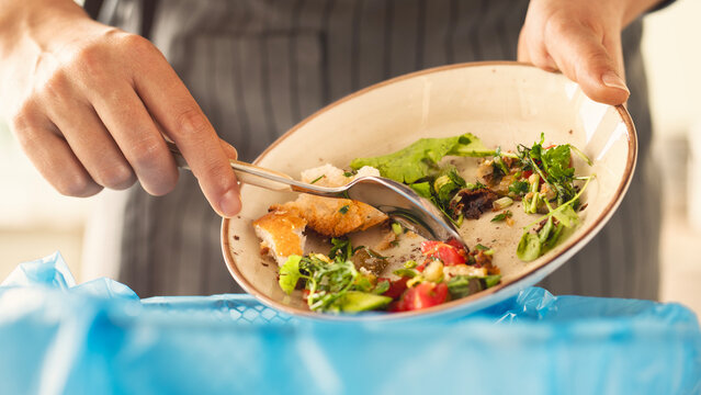 Woman scraping leftover food from plate into trash bin in kitchen