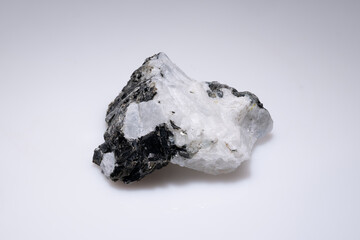 Raw moonstone specimen with black inclusions against a plain white background, showcasing its...