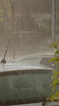 Vertical Screen: Hail and heavy rain batter the roof of a parked car in a city. The powerful storm produces splashes and possible damage due to the icy precipitation.