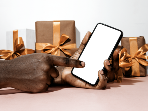 black hand holding pointing to white blank phone screen in his hand with gift boxes around. Mobile telephone mockup template	