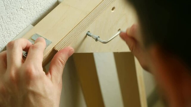 Hands expertly tighten bed frame bolts ensuring every part fits perfectly furniture. Hex key guides movement show dedication creating sturdy bed ready transform bedroom space. Assembling furniture