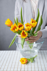 bouquet of tulips in glass vase. female florist puts yellow and red tulips in vase. birthday or mother's day gift. female florist collects a bouquet of flowers, casual clothes for a confident lady. 
