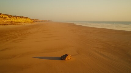 Serene beach landscape with a single rock on the golden sand